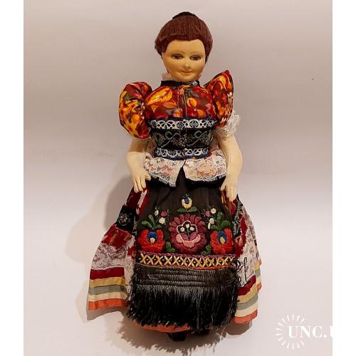 Старинная коллекционная кукла в национальной одежде, сидящая на стуле.